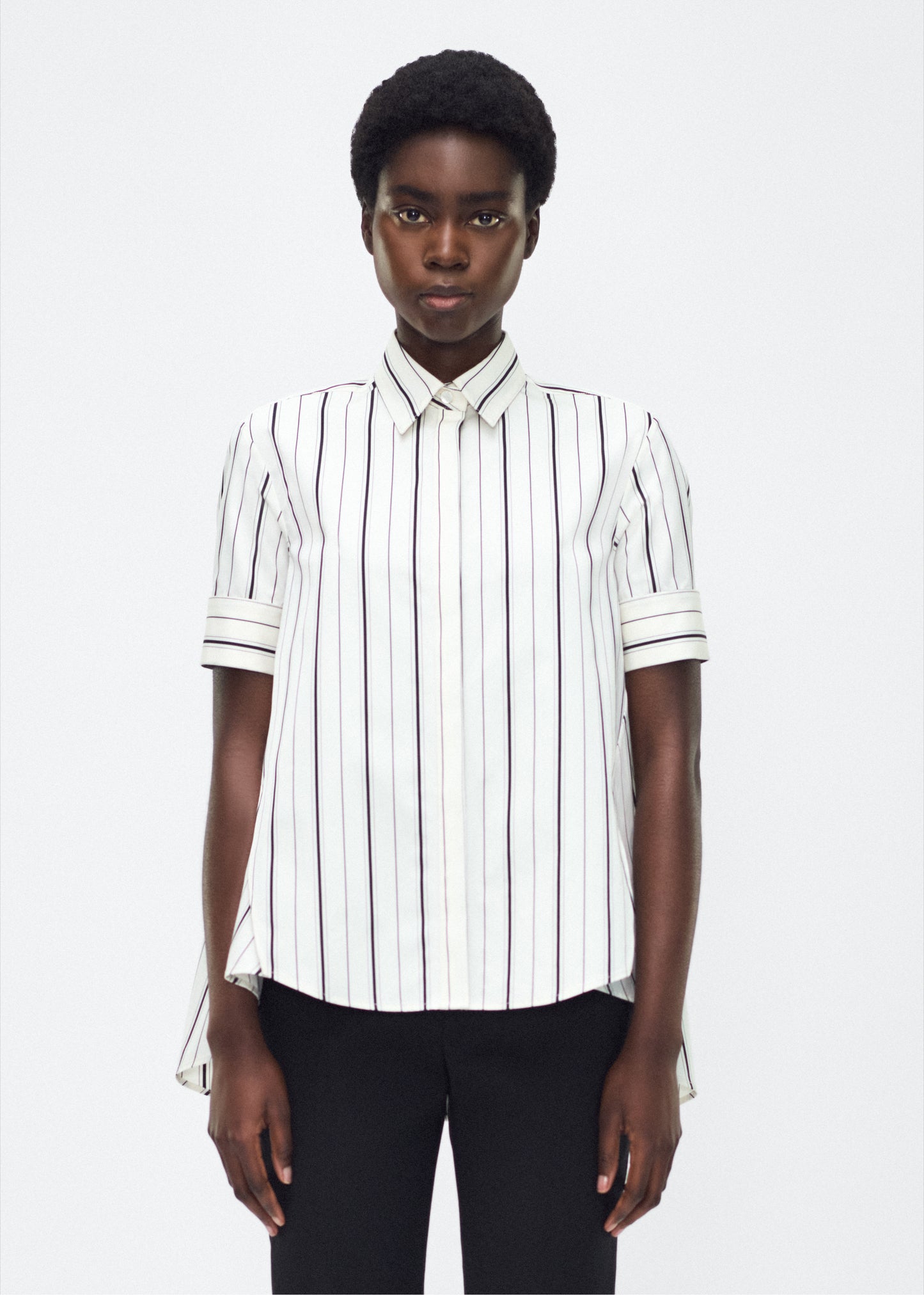 Model front facing image – Trapeze Shirt, P25106SS, Ivory/Black – Adam Lippes, P25 collection: The Adam Lippes Trapeze Shirt remains a timeless favorite from the atelier. Crafted from crisp Italian cotton, this season’s version features a classic ivory and black stripe. The piece features diamond monogram mother of pearl buttons along the center front placket, collar stand and French cuffs. Designed with side slits for a breezy, relaxed fit.