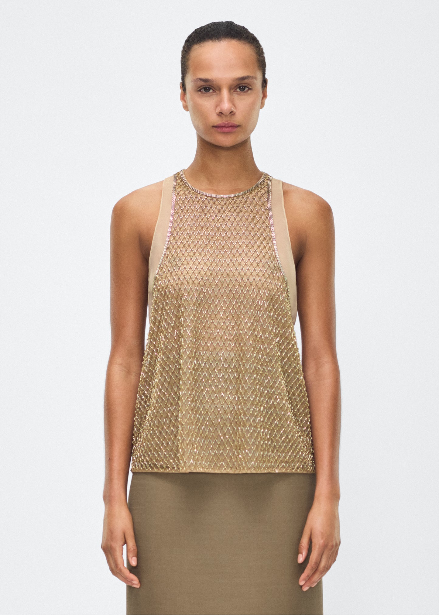 Image of model facing front – Fable Top, P25110TU, Gold – Adam Lippes, P25 collection: The Fable Top in beaded tulle features intricate glass beading, a meticulous hand-done process that takes several days, arranged in the signature diamond motif for a striking visual effect. This new shape from the atelier combines fine craftsmanship with a clean, modern silhouette.