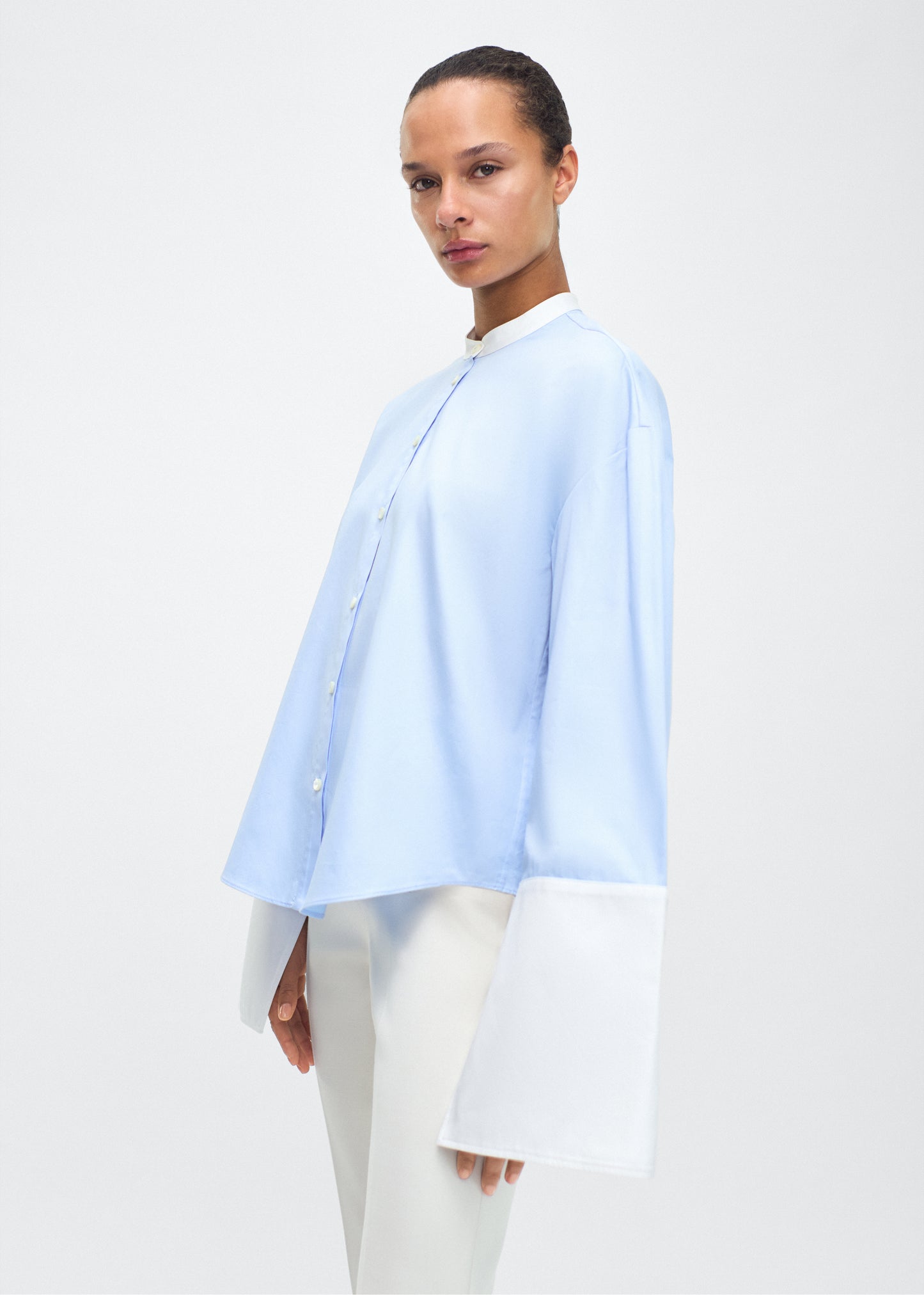 Ghost image angled forward – bram top, P25139CS, Pale Blue – Adam Lippes, P25 collection: A new shape from the atelier, the Bram Top is crafted from soft organic cotton poplin in a refreshing pale blue hue. The relaxed fit is enhanced by contrasting white cuffs and collar, with a subtle slit near the cuffs for added detail. Made from the highest quality cotton and featuring diamond monogram mother of pearl buttons down the center front, the top offers elegance and comfort.