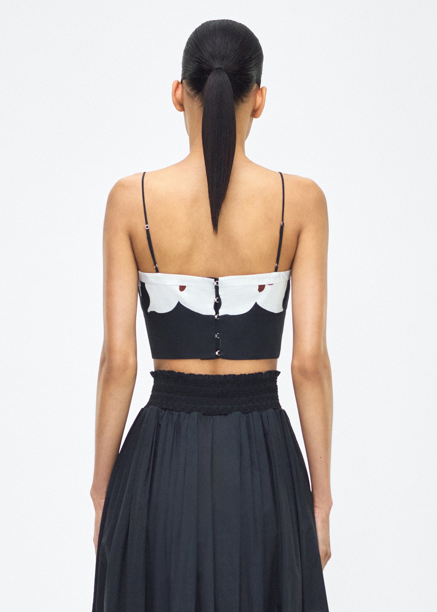 model facing back – bex top, P25143PV, black/white – Adam Lippes, P25 collection: Crafted from 100% cotton voile, the Bex Top showcases this season’s Sicily-inspired floral motif. The cropped silhouette offers a modern fit, while delicate straps and a clean neckline lend a minimalist touch.