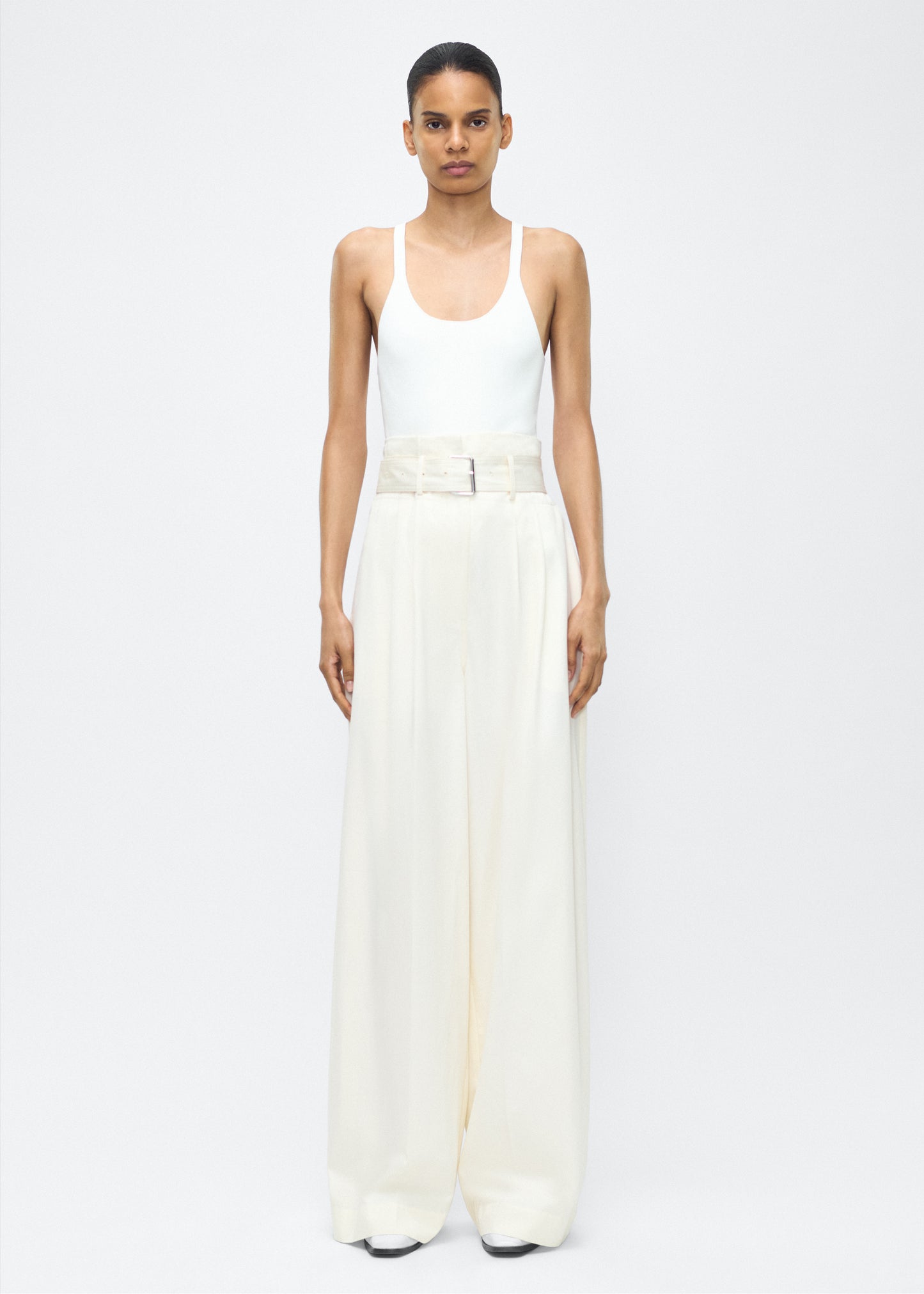 Image of model facing front – Jericho Pant, P25505WI, Ivory – Adam Lippes, P25 collection: The Jericho Pant is crafted from luxurious cotton-cashmere twill, offering the perfect balance of softness and structure. Pleated fronts and a wide-leg design create an easy, relaxed fit, while a belt at the waist adds elegant definition.