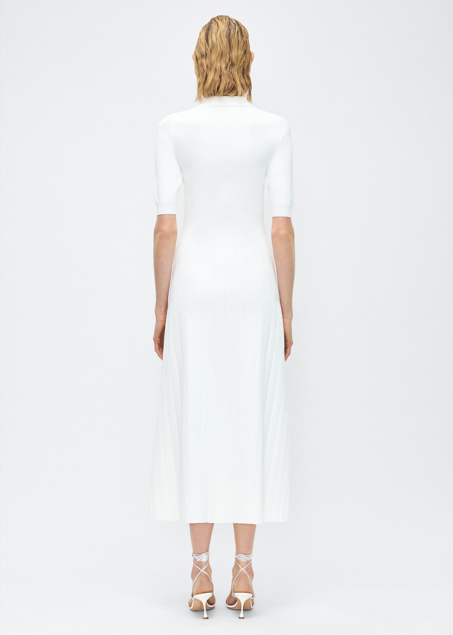 Model facing back – Fenwick Dress, P25626UB, Ivory – Adam Lippes, P25 collection: Crafted from a supple, ribbed knit, this dress skims the figure with ease, while an inset panel through the skirt introduces fluid movement. A button-down front and structured collar complete the look.