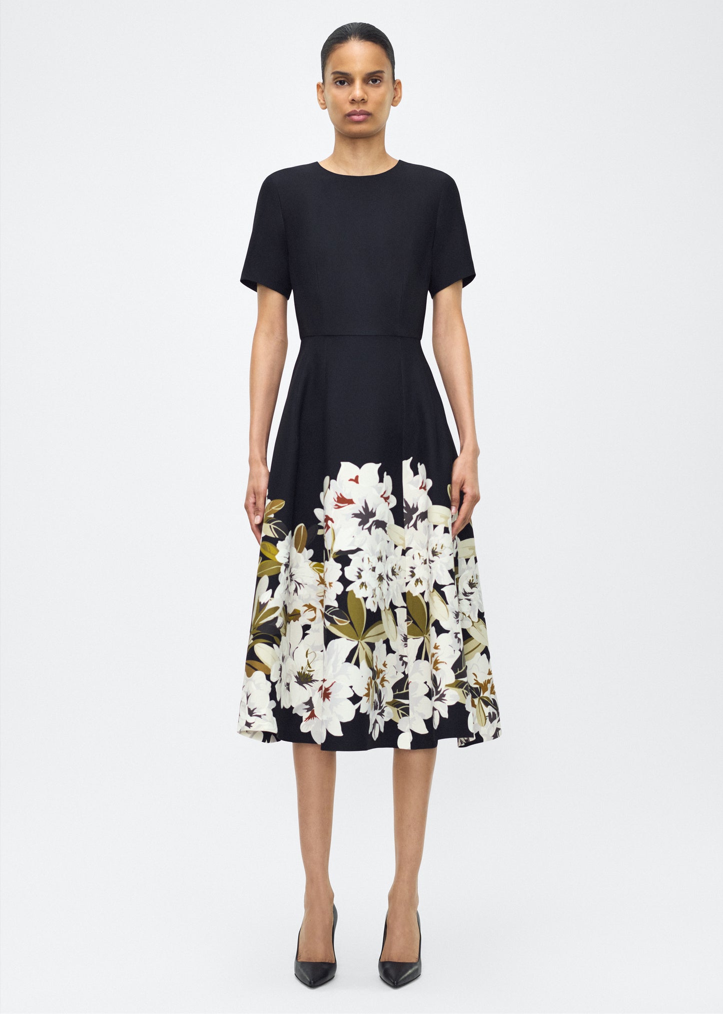Model facing front, wearing P25722PW, the Evangeline Dress in Black/white; From the Adam Lippes P25 Collection, A signature silhouette from the atelier, the Evangeline Dress is crafted in luxurious printed silk wool adorned with this season’s Sicily-inspired floral motif. Designed with an A-line silhouette and a gently flared skirt, it drapes gracefully for an elegant look.
