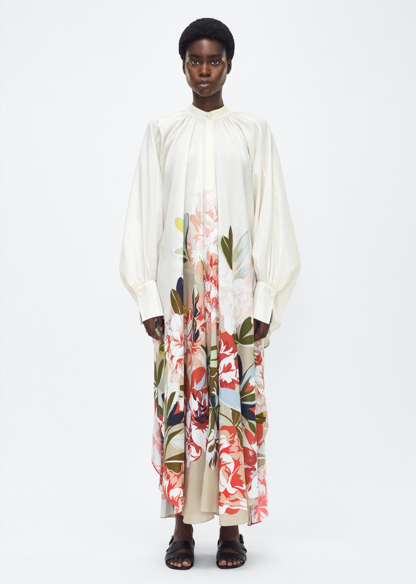 Model facing front, P25726PV, Rysa Caftan, Champagne/Multi, Adam Lippes P25 Collection; A new shape from the atelier, the Rysa Caftan is crafted from airy printed voile, featuring this season’s Sicily-inspired floral motif. The fluid hem adds a modern twist to the traditional caftan silhouette. With its flowing, relaxed fit, it exudes effortless elegance. Features a button loop closure and diamond monogram mother of pearl buttons.