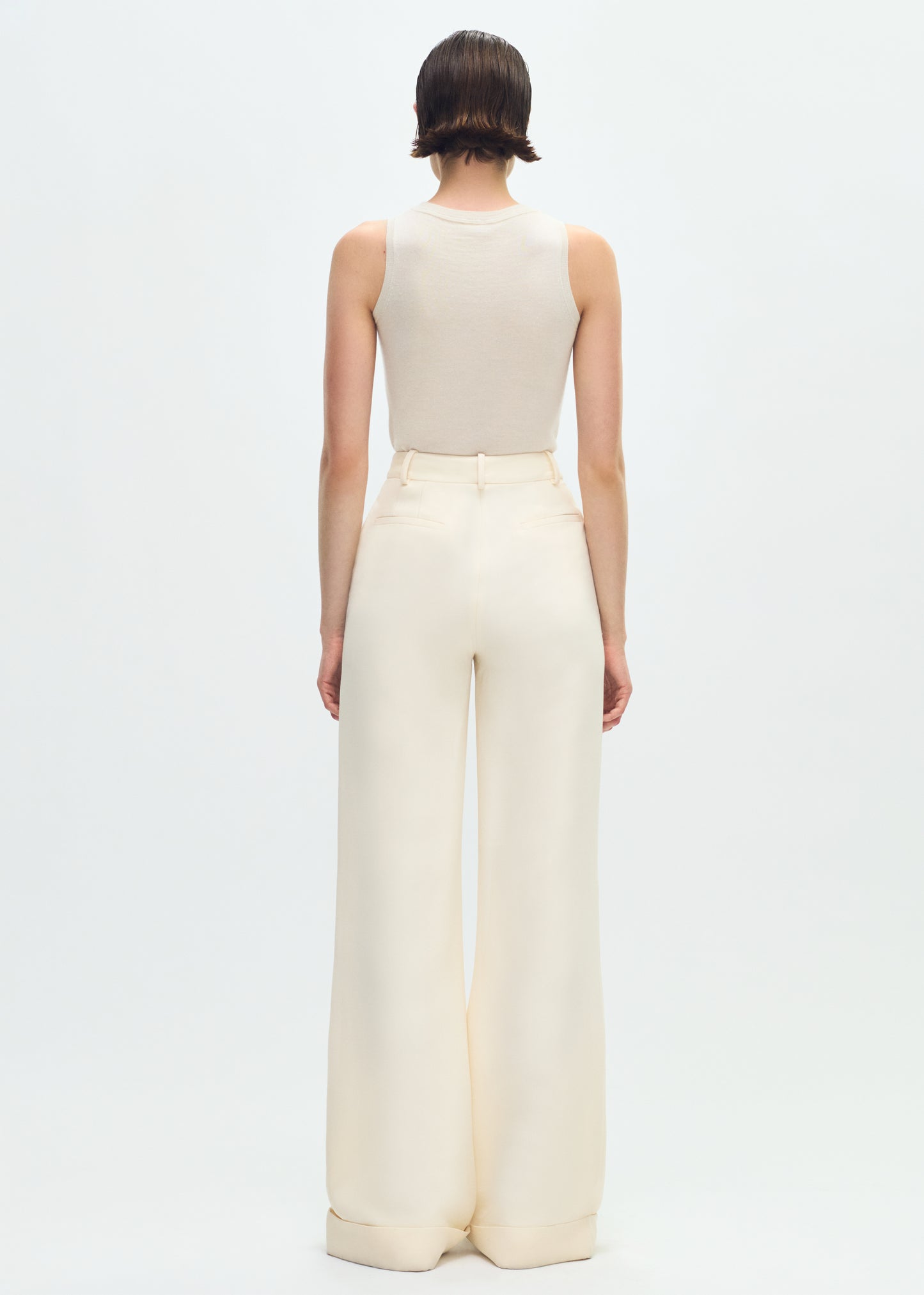 Image of a model facing backwards wearing ivory tank tucked into ivory pants.