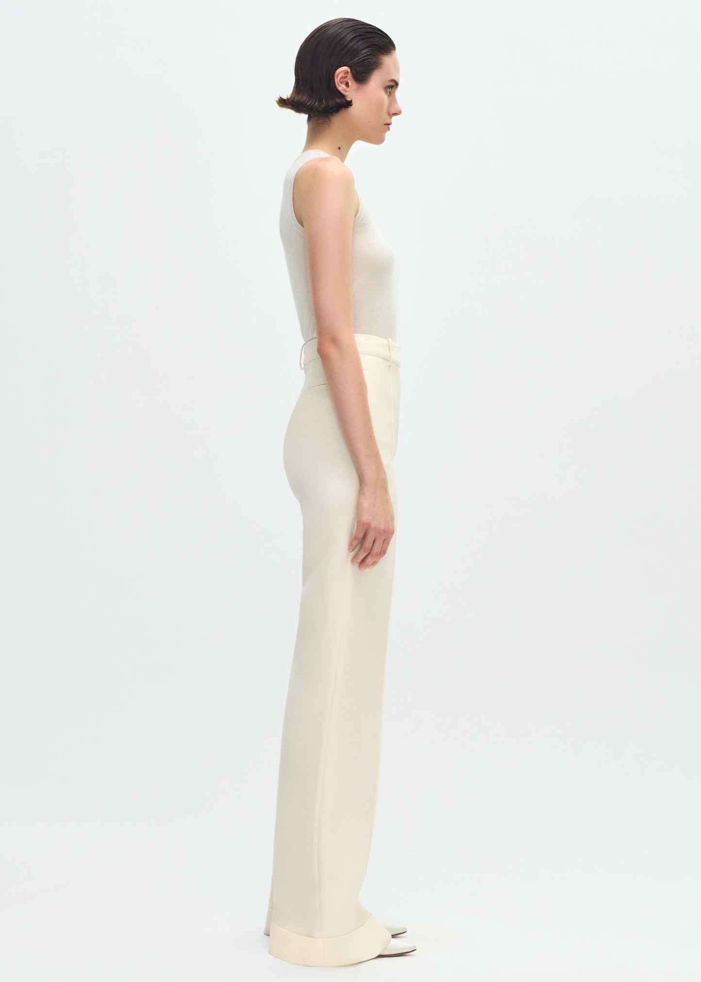 Image of a model facing sideways wearing a white tank tucked into ivory pants.