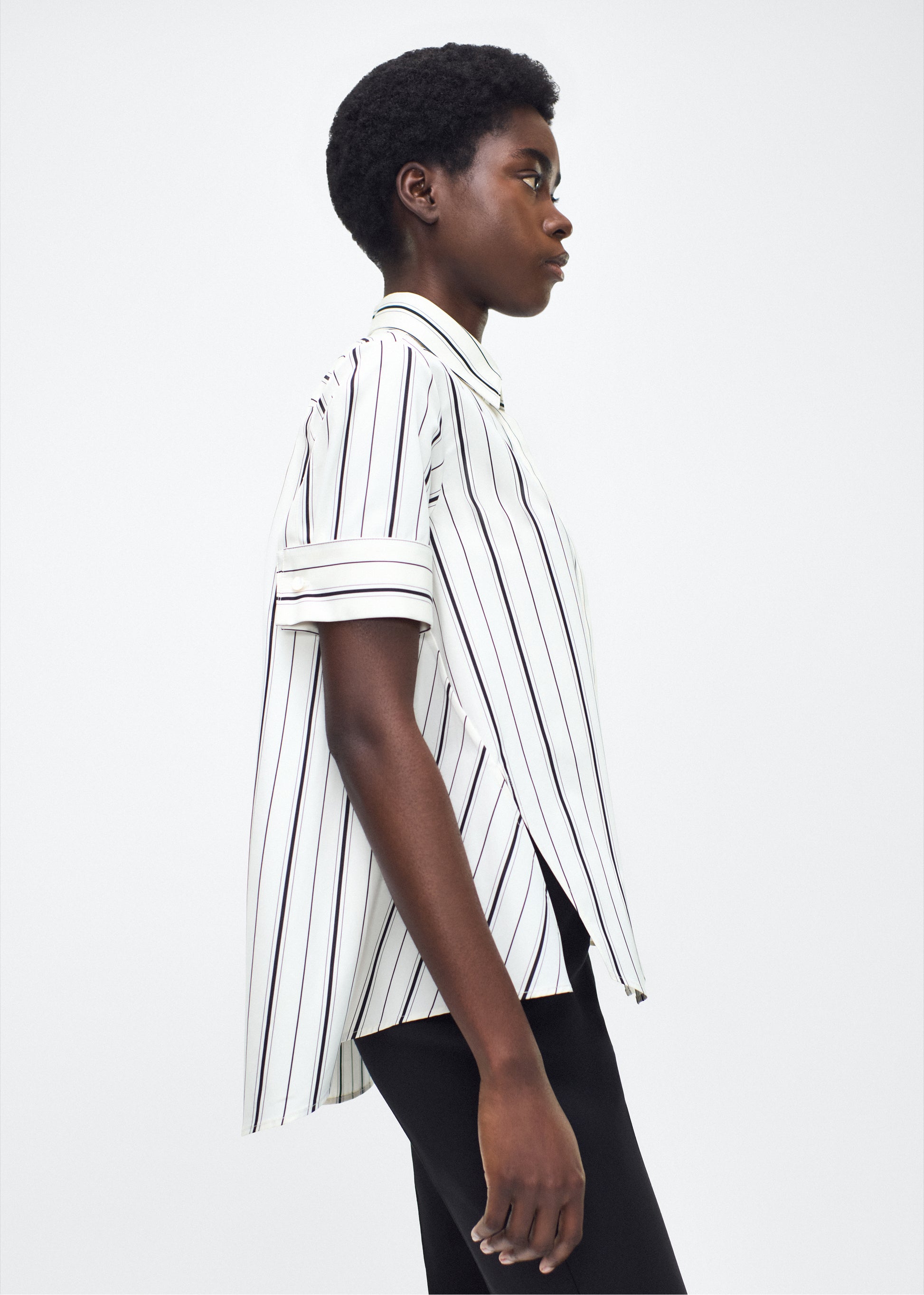 Model side facing image – Trapeze Shirt, P25106SS, Ivory/Black – Adam Lippes, P25 collection: The Adam Lippes Trapeze Shirt remains a timeless favorite from the atelier. Crafted from crisp Italian cotton, this season’s version features a classic ivory and black stripe. The piece features diamond monogram mother of pearl buttons along the center front placket, collar stand and French cuffs. Designed with side slits for a breezy, relaxed fit.