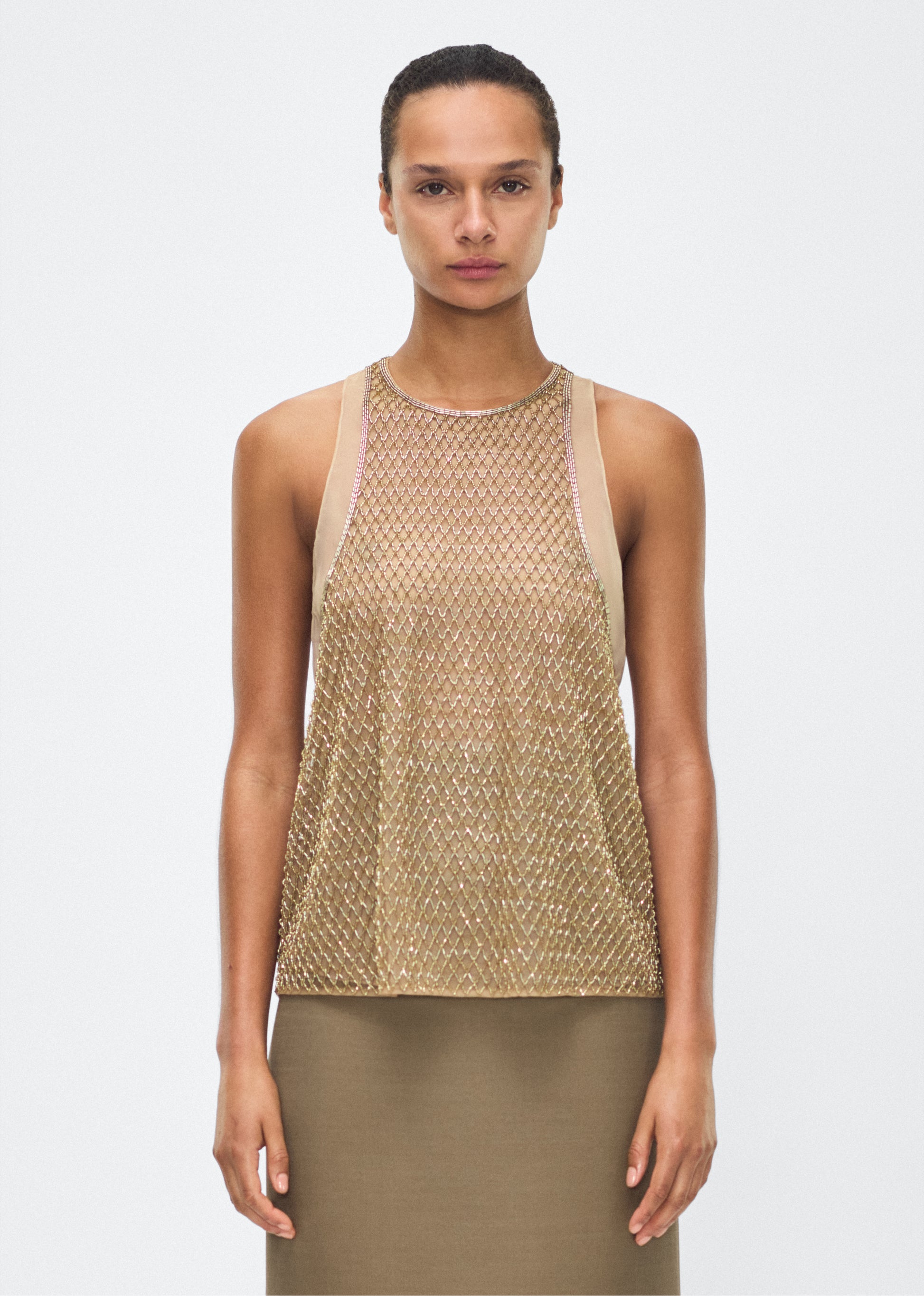 Image of model facing front – Fable Top, P25110TU, Gold – Adam Lippes, P25 collection: The Fable Top in beaded tulle features intricate glass beading, a meticulous hand-done process that takes several days, arranged in the signature diamond motif for a striking visual effect. This new shape from the atelier combines fine craftsmanship with a clean, modern silhouette.