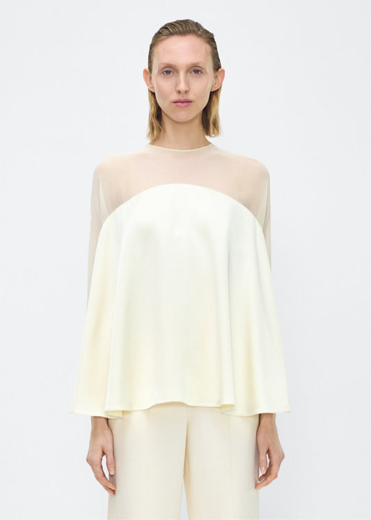 Model facing front – apollo top, P25127DC, cream – Adam Lippes, P25 collection: A new shape from the atelier, the Apollo Top is crafted from luxurious 100% silk in a soft cream hue. The flowing, draped design features a high-neck collar and a cascading silhouette, exuding modern elegance. 