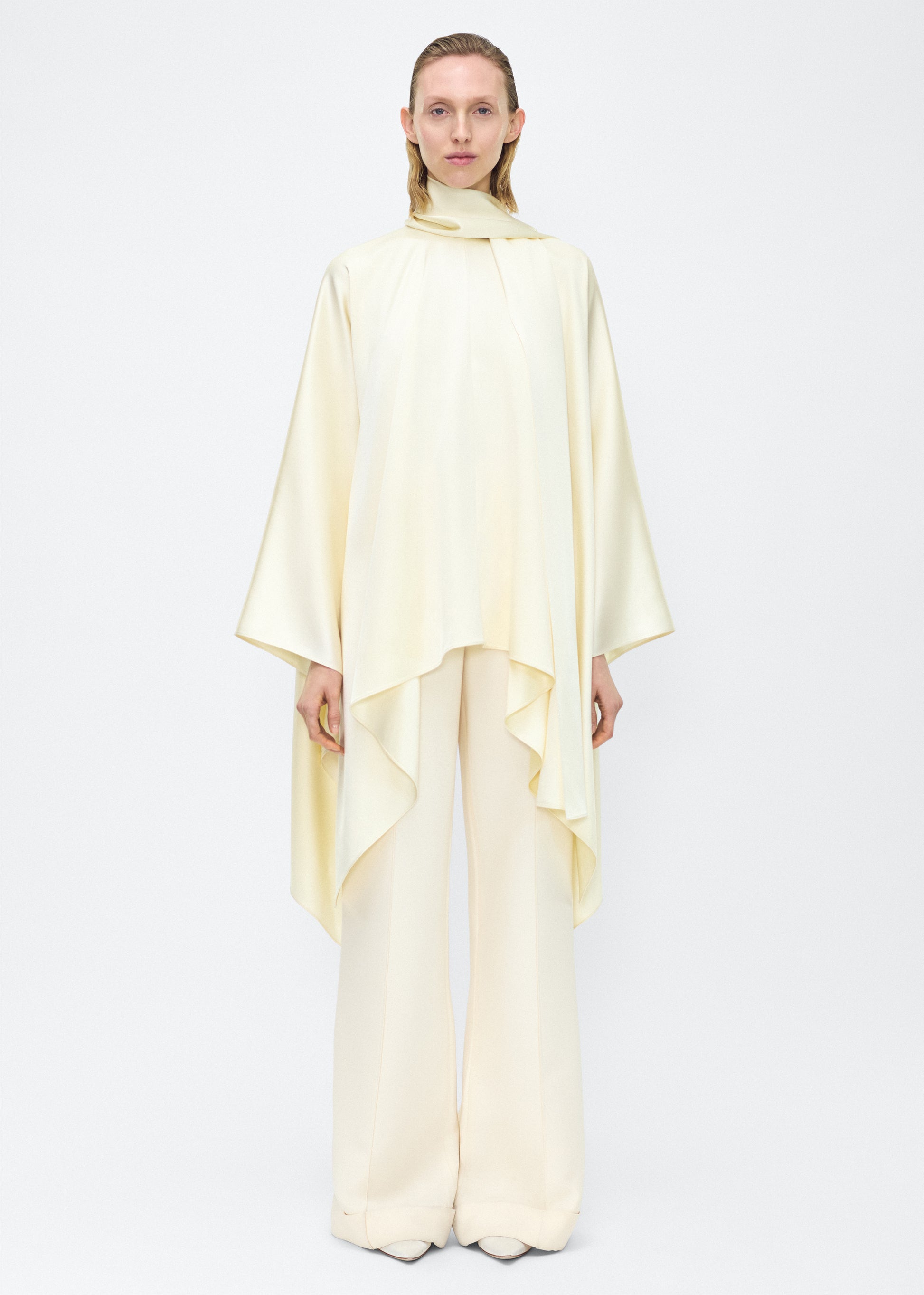 Model facing front – tana top , P25134HM, cream – Adam Lippes, P25 collection: The Tana Top is crafted from luxurious double-face charmeuse, offering a rich, fluid drape in a delicate cream hue. Featuring a detachable scarf for versatile styling options. The clean lines and elegant shape make it a statement piece, perfect for both dressing up and down.