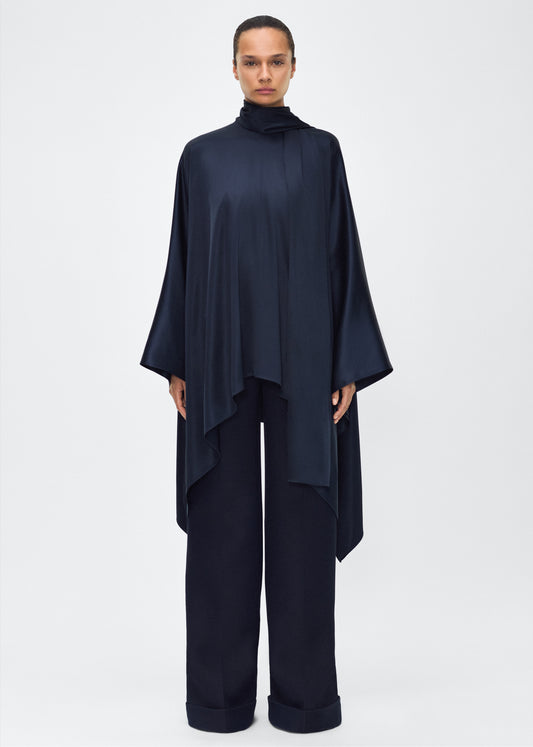 Model facing front – tana top , P25134HM, Navy – Adam Lippes, P25 collection: The Tana Top is crafted from luxurious double-face charmeuse, offering a rich, fluid drape in a delicate cream hue. Featuring a detachable scarf for versatile styling options. The clean lines and elegant shape make it a statement piece, perfect for both dressing up and down.