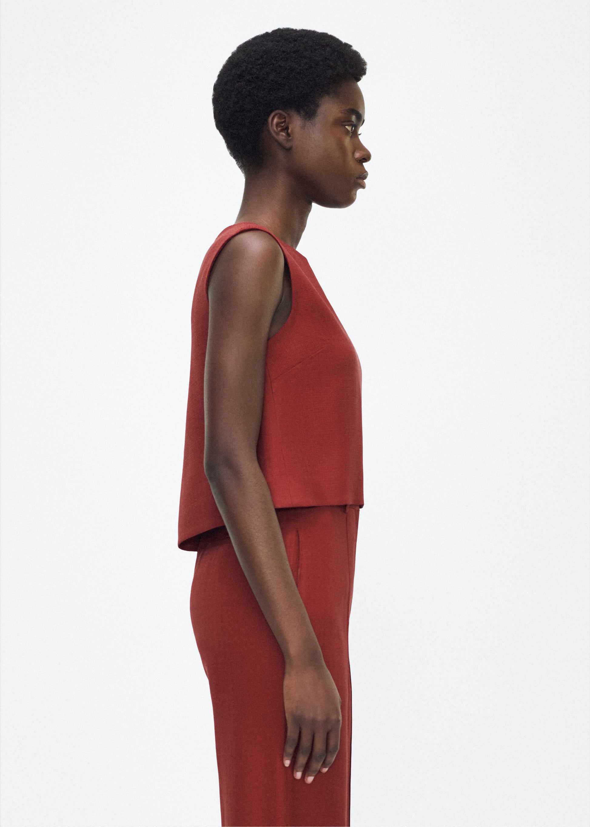 Image of model facing side mercer top, P25144TR, sienna – Adam Lippes, P25 collection: This cropped-silhouette top is crafted from stretch canvas in a rich sienna hue, offering a perfect balance of softness and structure. A box pleat at the back adds subtle, refined shape.