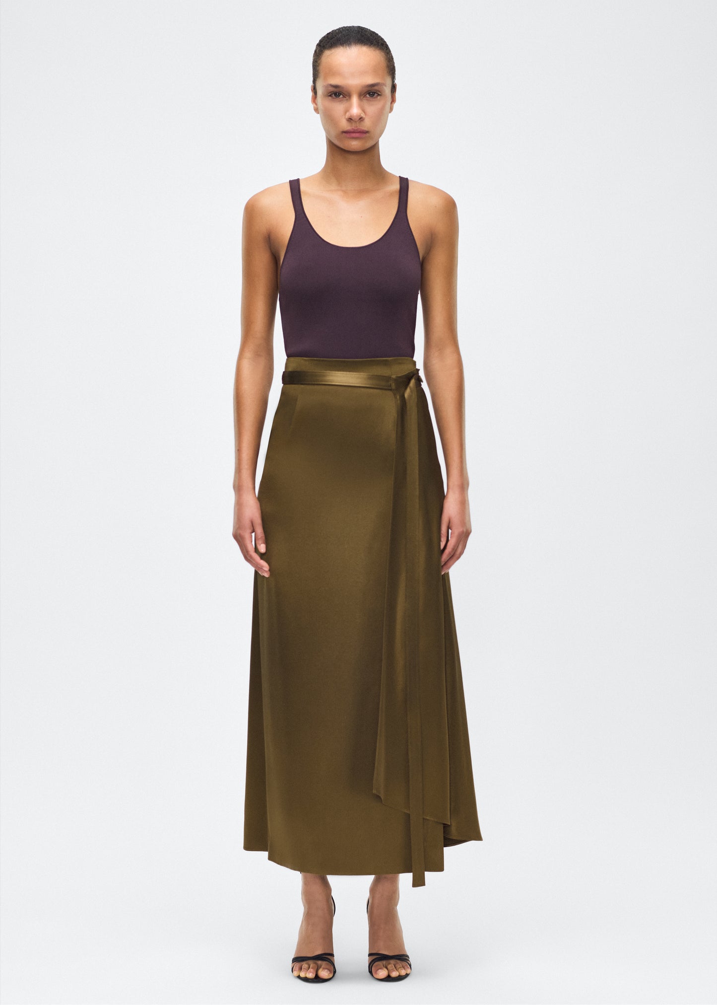 model image front – bruna skirt, P25403HM, olive – Adam Lippes, P25 collection: The Bruna Skirt is crafted from luxurious double-face silk charmeuse, offering a rich sheen and fluid drape. Rendered in a deep olive hue, cascading fabric at the side of the piece adds subtle movement to the elegant silhouette. 
