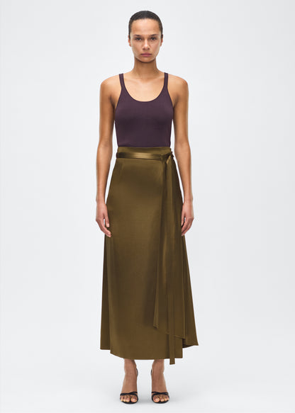 model image front – bruna skirt, P25403HM, olive – Adam Lippes, P25 collection: The Bruna Skirt is crafted from luxurious double-face silk charmeuse, offering a rich sheen and fluid drape. Rendered in a deep olive hue, cascading fabric at the side of the piece adds subtle movement to the elegant silhouette. 