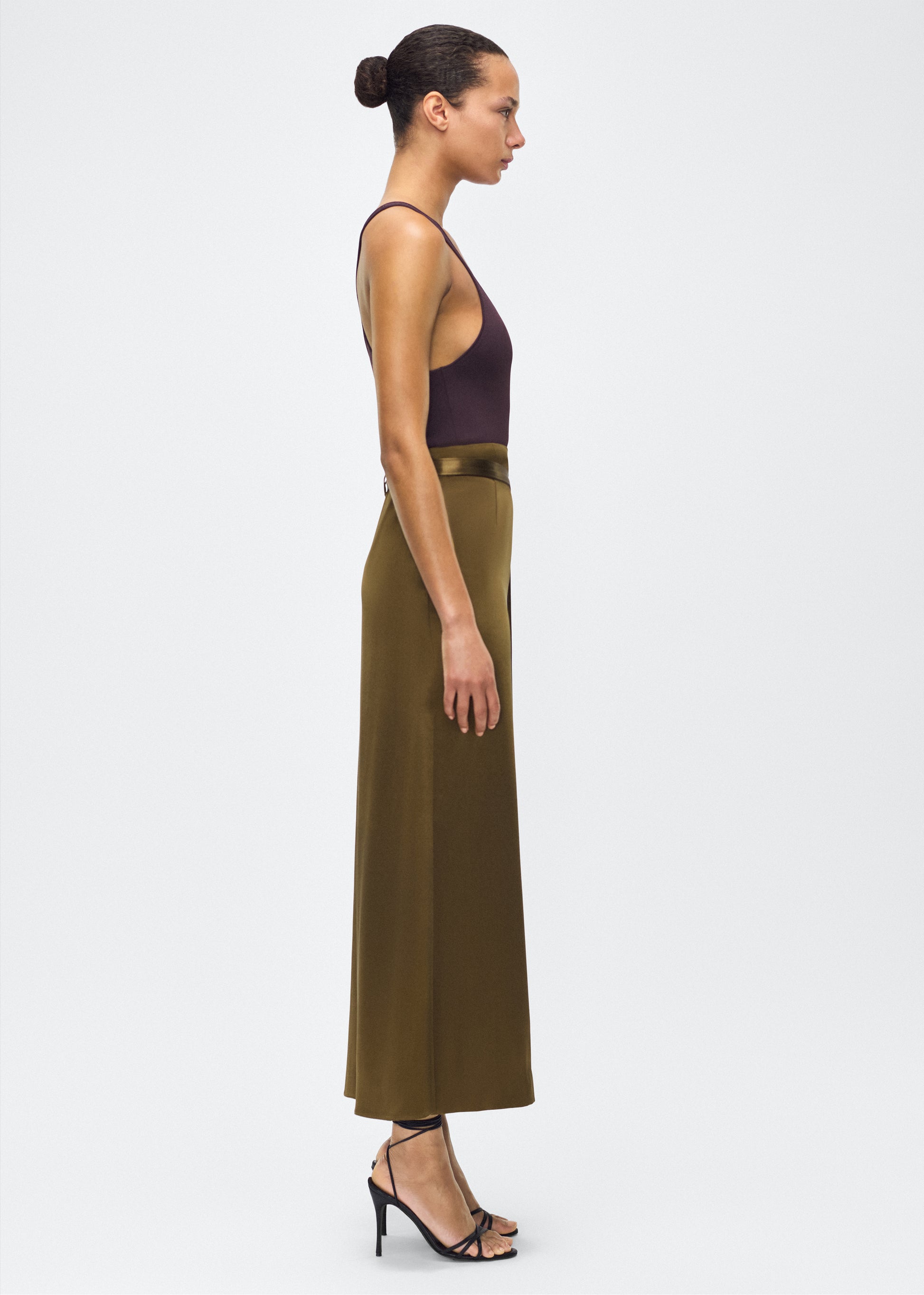 model image side – bruna skirt, P25403HM, olive – Adam Lippes, P25 collection: The Bruna Skirt is crafted from luxurious double-face silk charmeuse, offering a rich sheen and fluid drape. Rendered in a deep olive hue, cascading fabric at the side of the piece adds subtle movement to the elegant silhouette. 