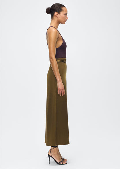 model image side – bruna skirt, P25403HM, olive – Adam Lippes, P25 collection: The Bruna Skirt is crafted from luxurious double-face silk charmeuse, offering a rich sheen and fluid drape. Rendered in a deep olive hue, cascading fabric at the side of the piece adds subtle movement to the elegant silhouette. 