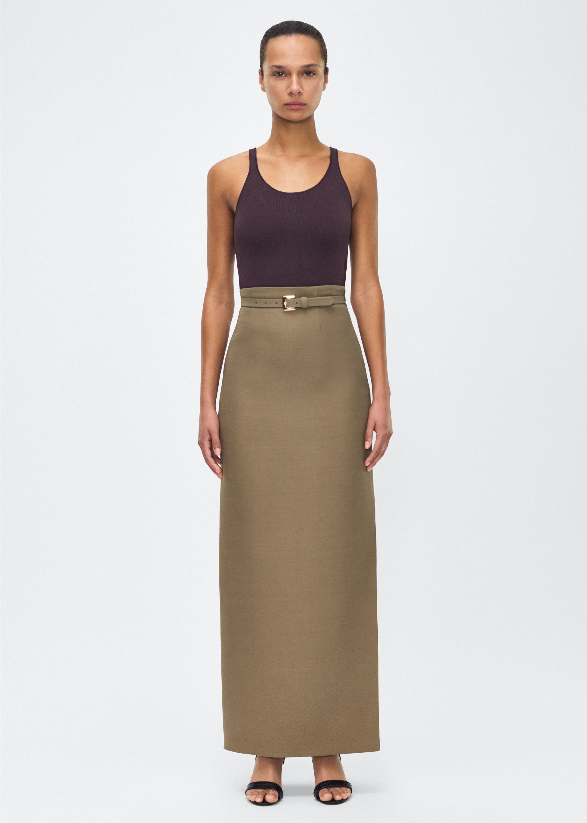 Model facing front wearing Leto Skirt, P25412SW, Military Green – Adam Lippes, P25 collection:The Leto Skirt offers an elevated pencil silhouette, crafted from luxurious silk wool in a sophisticated military green hue. The sleek design is accentuated by a fabric-covered belt, cinching the waist for a tailored fit.
