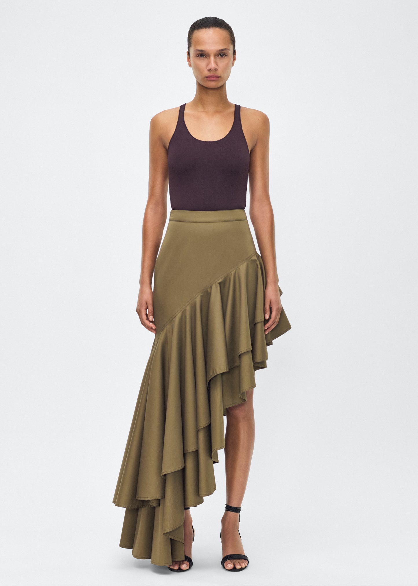 Model facing front – Cortes Skirt, P25413CT, Military Green – Adam Lippes, P25 collection: A new shape from the atelier, the Cortés Skirt is crafted from cotton twill in a rich military green hue. Featuring a dramatic asymmetrical ruffle, this skirt adds dynamic movement and texture. The high-waisted fit and expertly placed ruffles make it a statement piece that effortlessly transitions from day to night.
