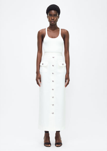 Image of model facing the front – Dakota Skirt, P25417WN, White – Adam Lippes, P25 collection: This classic skirt, crafted from Italian white denim, features elegant silver buttons cast with our iconic diamond monogram along the center front and functional front pockets. Featuring an invisible zipper for elegant wear, the tailored waist creates a defined silhouette. Pair with the Remo Top in White Denim for a complete look.