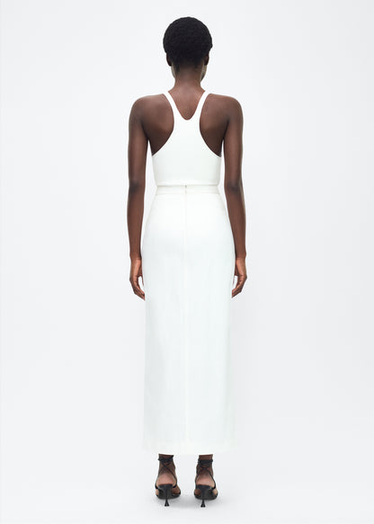 Image of model facing the back – Dakota Skirt, P25417WN, White – Adam Lippes, P25 collection: This classic skirt, crafted from Italian white denim, features elegant silver buttons cast with our iconic diamond monogram along the center front and functional front pockets. Featuring an invisible zipper for elegant wear, the tailored waist creates a defined silhouette. Pair with the Remo Top in White Denim for a complete look.