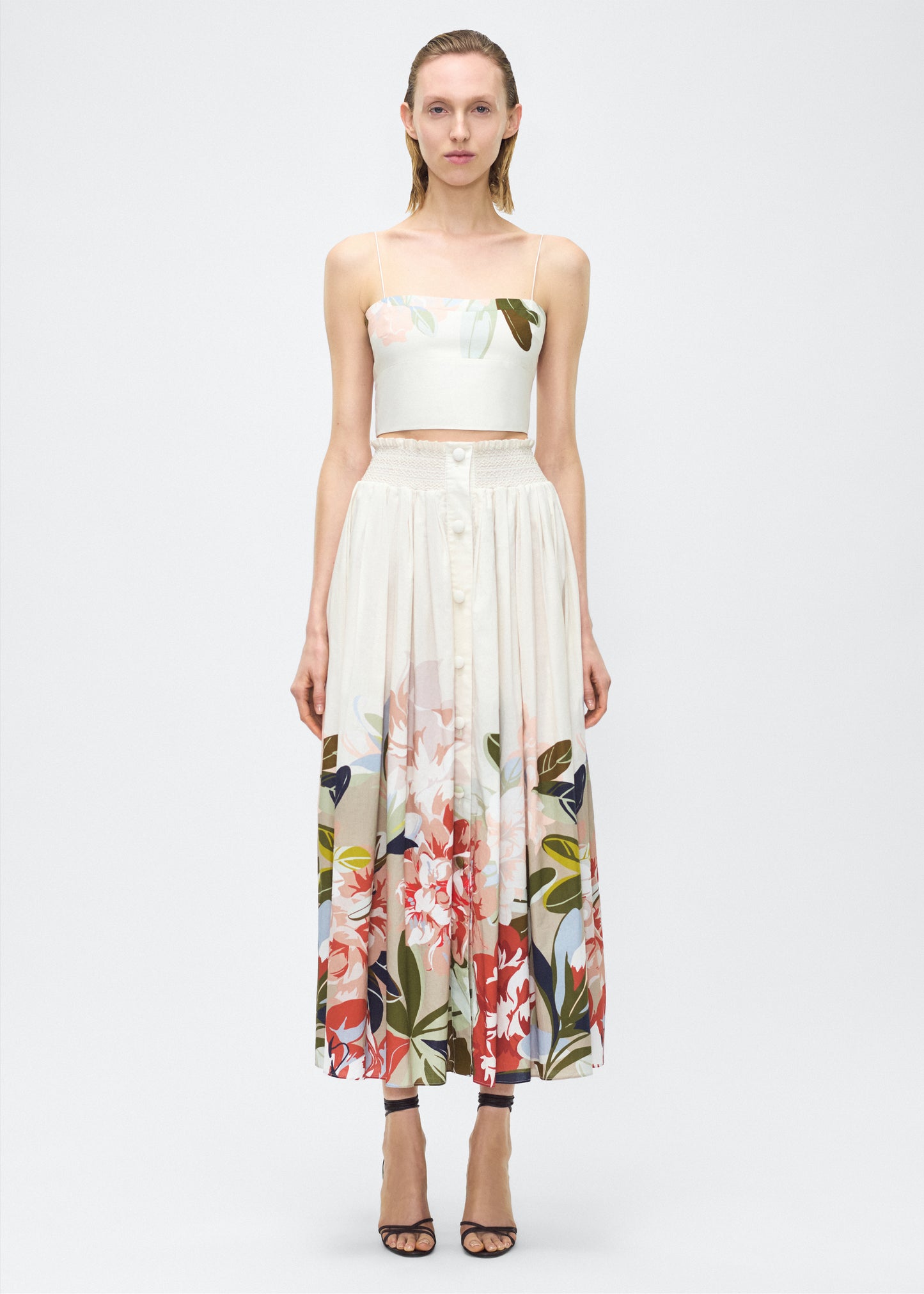 Image of model front– Lovisa Skirt, P25418PV, Champagne Multi – Adam Lippes, P25 collection: A signature shape from the atelier, the Lovisa Skirt is crafted from airy printed voile featuring a vibrant Sicily-inspired floral motif. Designed with a smocked waistband for a comfortable fit, the skirt is finished with fabric-covered buttons down the center front. Pair with the Bex Top in Printed Voile for a coordinated look.