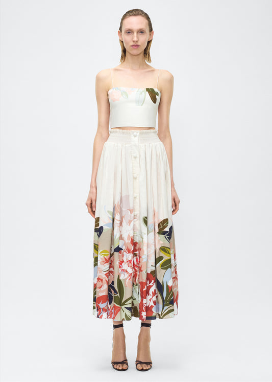 Image of model front– Lovisa Skirt, P25418PV, Champagne Multi – Adam Lippes, P25 collection: A signature shape from the atelier, the Lovisa Skirt is crafted from airy printed voile featuring a vibrant Sicily-inspired floral motif. Designed with a smocked waistband for a comfortable fit, the skirt is finished with fabric-covered buttons down the center front. Pair with the Bex Top in Printed Voile for a coordinated look.