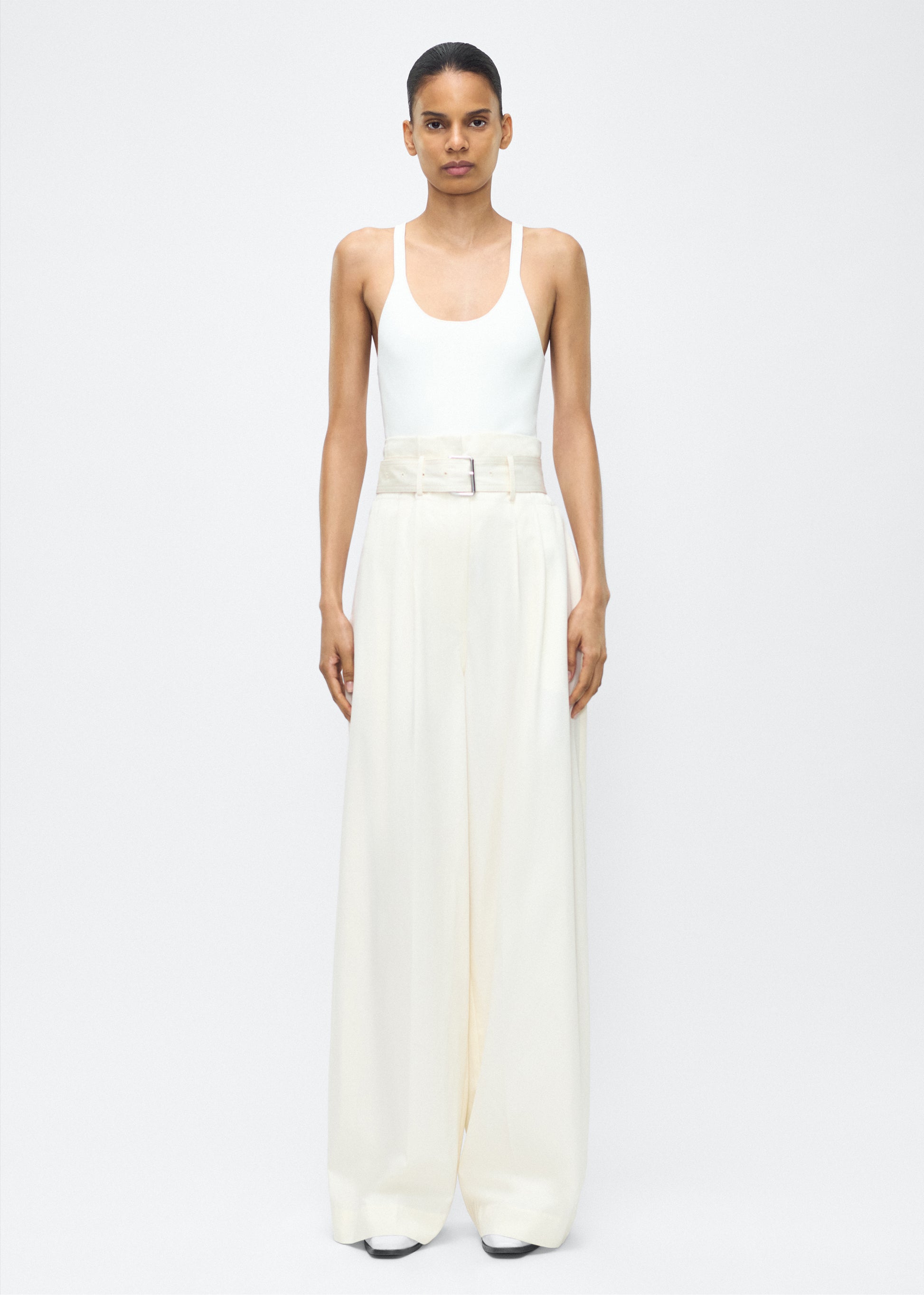 Image of model facing front – Jericho Pant, P25505WI, Ivory – Adam Lippes, P25 collection: The Jericho Pant is crafted from luxurious cotton-cashmere twill, offering the perfect balance of softness and structure. Pleated fronts and a wide-leg design create an easy, relaxed fit, while a belt at the waist adds elegant definition.