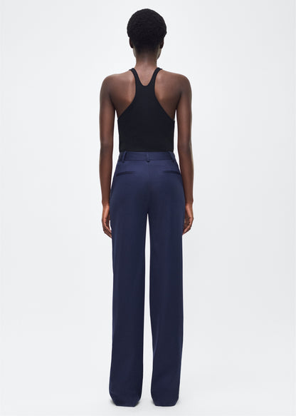 Image of model facing backwards wearing the Wyatt Pant, P25507TW, Navy – Adam Lippes, P25 collection: Precision tailoring meets warm-weather ease in the Wyatt Pant, now rendered in lightweight tropical wool. Cut in a deep navy hue, the silhouette is sleek and elongating, with a high-rise waist and fluid shape ideal for refined summer dressing.