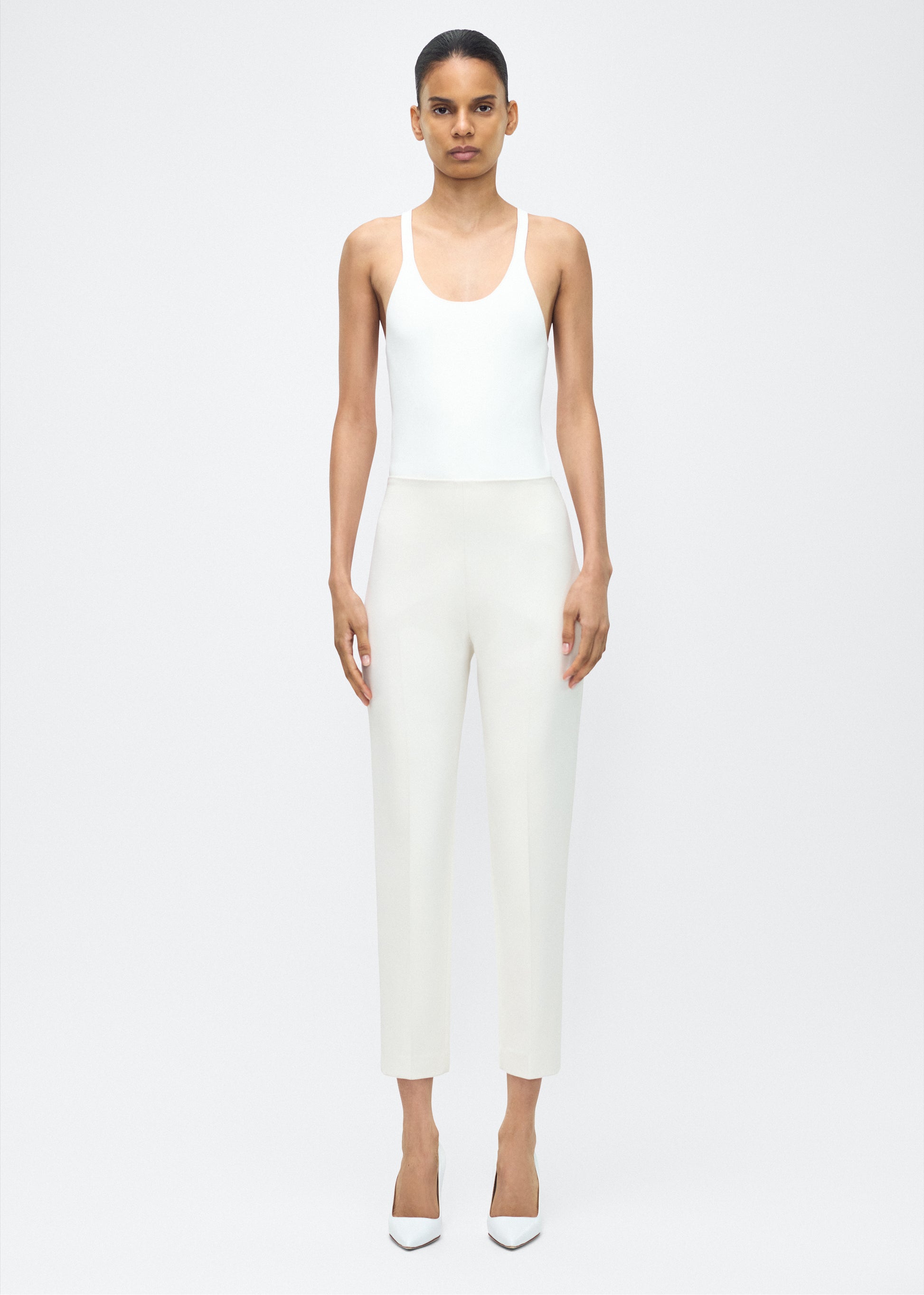 Model facing forward wearing – Kit Pant, P25512VT, Ivory – Adam Lippes, P25 collection: The Kit Pant introduces a sleek new silhouette, impeccably tailored in compact viscose. Designed to contour the legs, this ankle-grazing pant delivers effortless polish and modern ease.