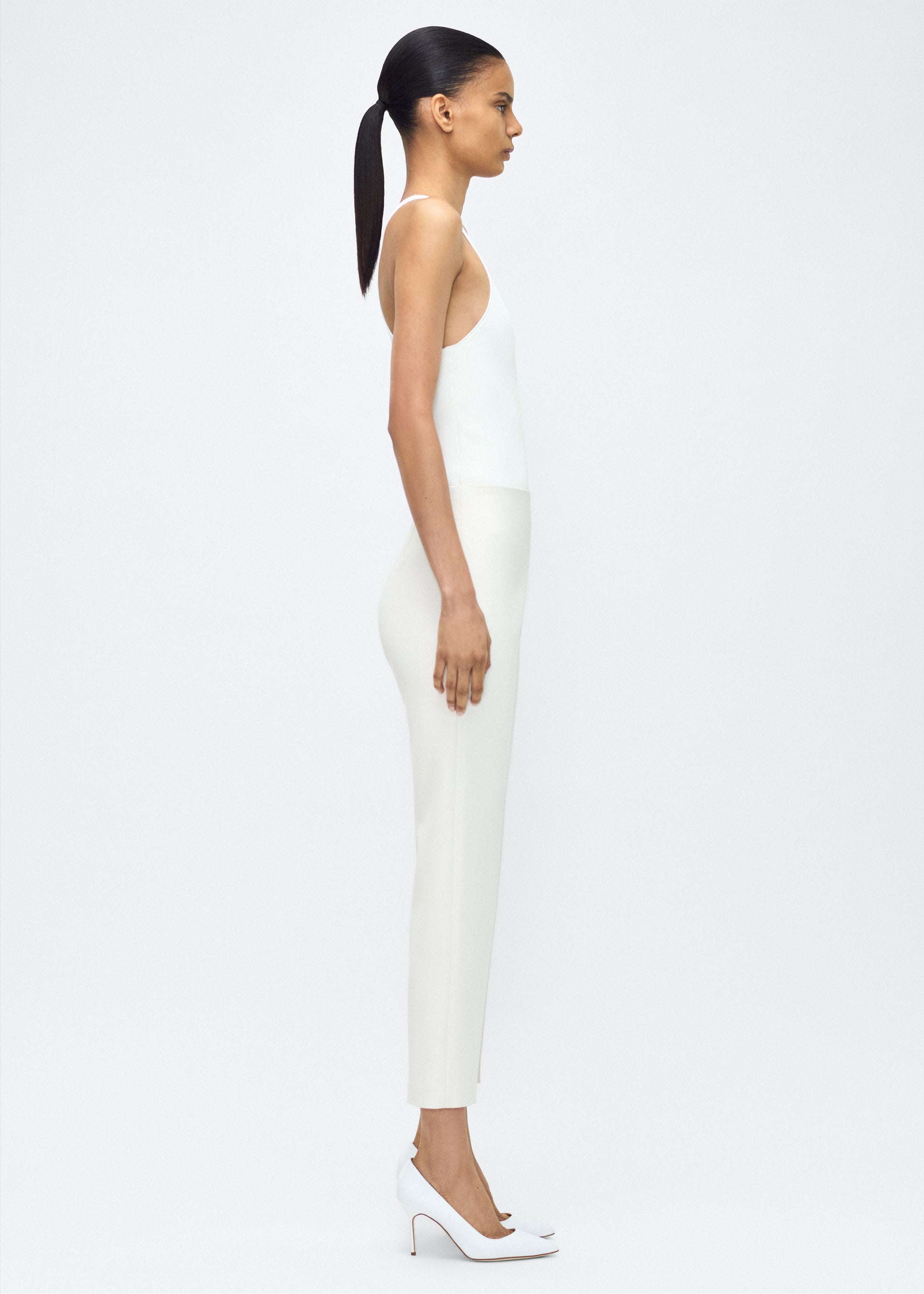 Model facing sideways wearing – Kit Pant, P25512VT, Ivory – Adam Lippes, P25 collection: The Kit Pant introduces a sleek new silhouette, impeccably tailored in compact viscose. Designed to contour the legs, this ankle-grazing pant delivers effortless polish and modern ease.