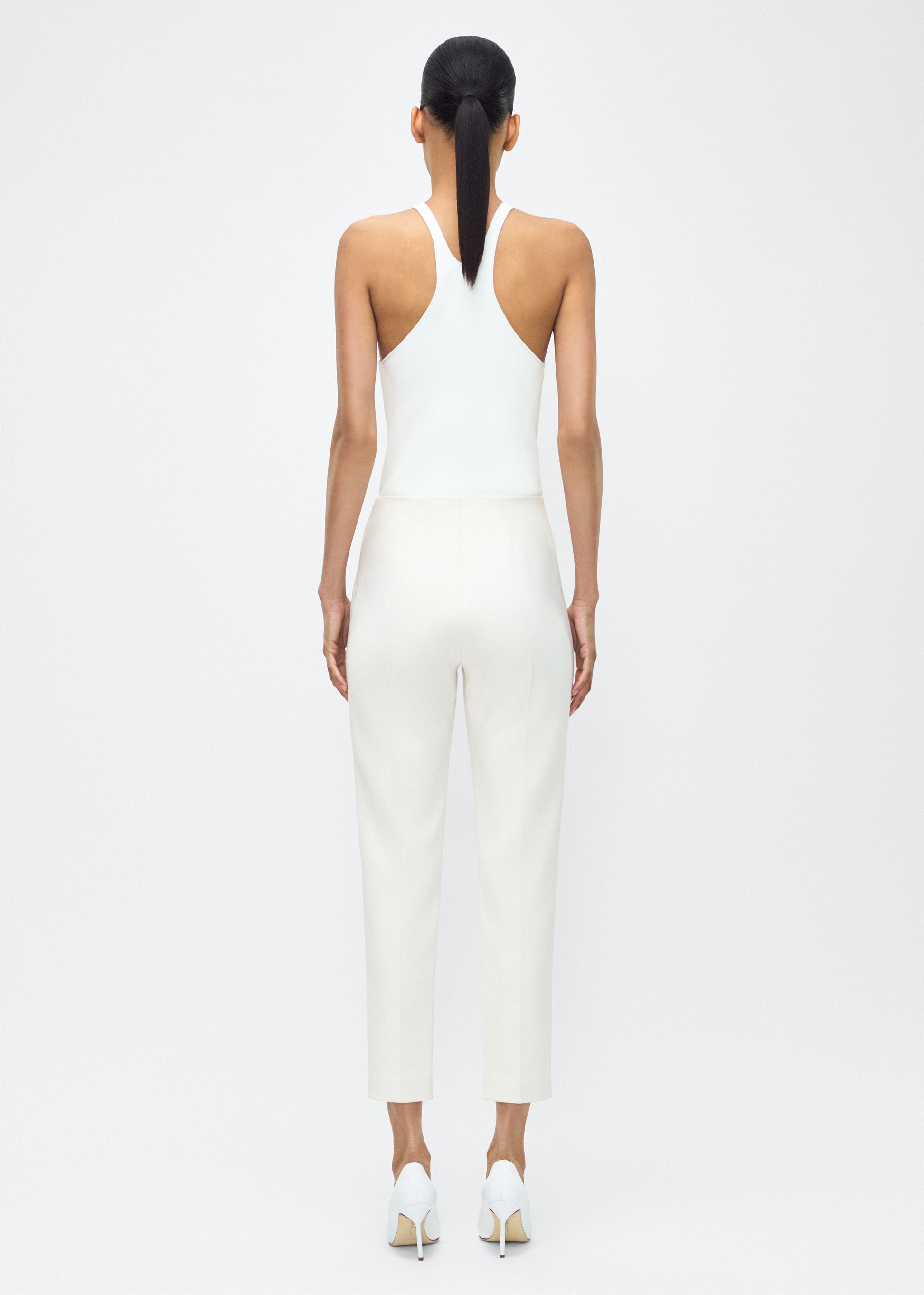 Model facing back wearing – Kit Pant, P25512VT, Ivory – Adam Lippes, P25 collection: The Kit Pant introduces a sleek new silhouette, impeccably tailored in compact viscose. Designed to contour the legs, this ankle-grazing pant delivers effortless polish and modern ease.
