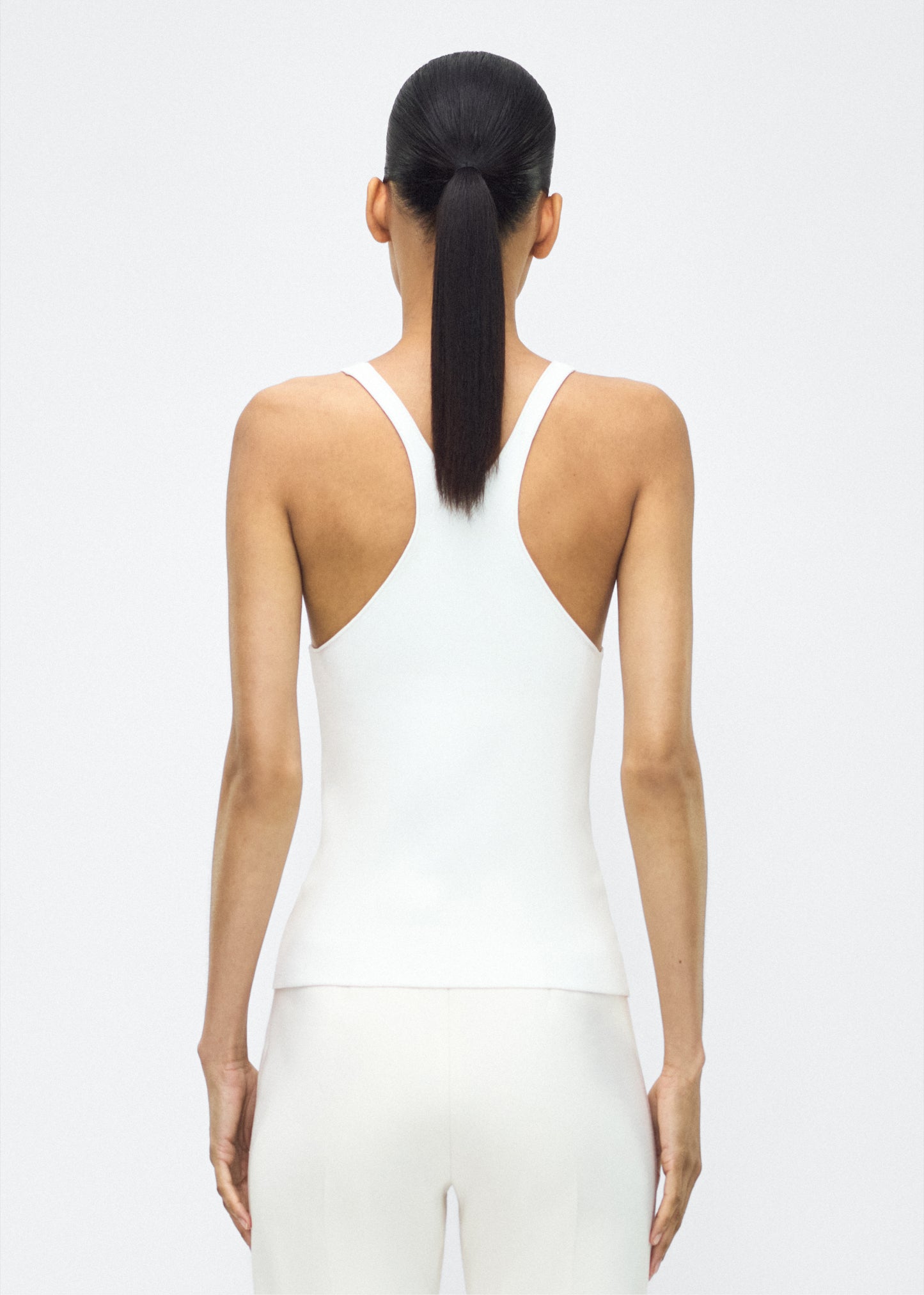 Image of model facing the back lumii tank , P25601VI, ivory – Adam Lippes, P25 collection:A new silhouette from the atelier, the Lumii Tank is crafted from luxurious knitted viscose. Clean lines and athletic-inspired straps make it a versatile piece for layering or wearing alone.