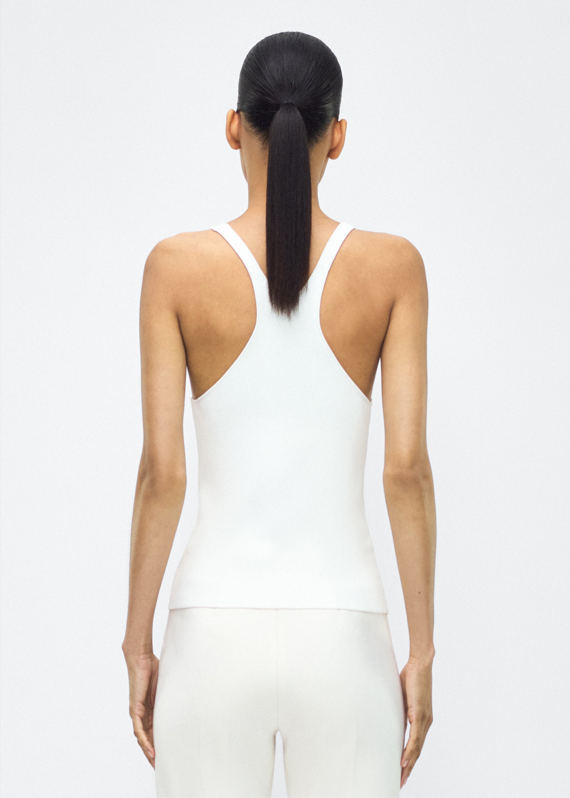 Image of model facing the back lumii tank , P25601VI, ivory – Adam Lippes, P25 collection:A new silhouette from the atelier, the Lumii Tank is crafted from luxurious knitted viscose. Clean lines and athletic-inspired straps make it a versatile piece for layering or wearing alone.
