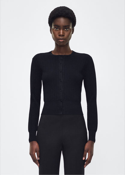 Image of model facing front, P25625UB, Faye Cardigan in black, Adam Lippes P25 collection: A classic pointelle stitch cardigan, crafted in our signature compact jacquard. Designed with a fitted bodice and delicate stitching, the piece is finished with covered buttons along the front placket for a refined look.
