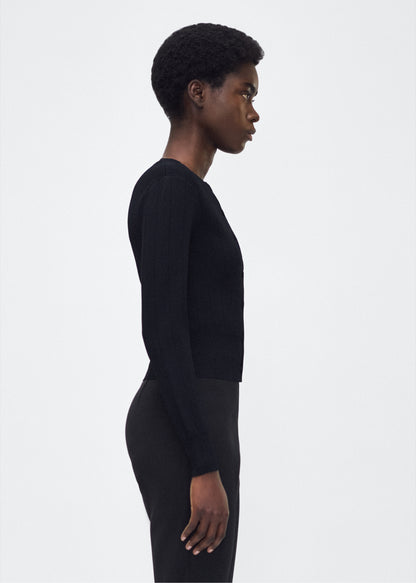 Image of model facing side P25625UB, Faye Cardigan in black, Adam Lippes P25 collection: A classic pointelle stitch cardigan, crafted in our signature compact jacquard. Designed with a fitted bodice and delicate stitching, the piece is finished with covered buttons along the front placket for a refined look.