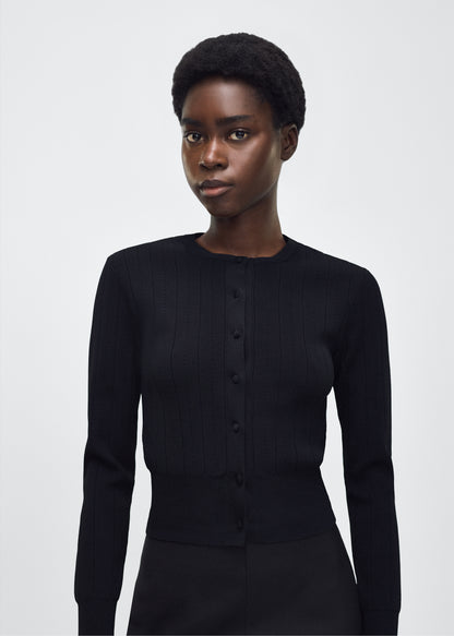 Image of model facing front, P25625UB, Faye Cardigan in black, Adam Lippes P25 collection: A classic pointelle stitch cardigan, crafted in our signature compact jacquard. Designed with a fitted bodice and delicate stitching, the piece is finished with covered buttons along the front placket for a refined look.