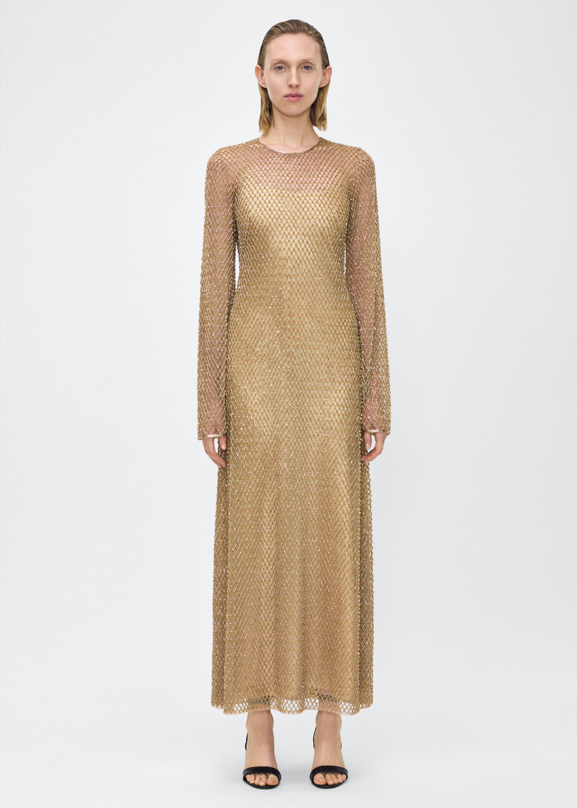 Model facing front, Image of the Sylvia Dress in Gold, P25 Adam Lippes collection; The Sylvia Dress in gold glass beaded tulle features intricate hand-beading, a process that takes multiple days, arranged in the signature diamond motif pattern for a striking visual effect. Designed with an elegant open back and a detachable cami, this dress offers versatile styling options with maximum impact.