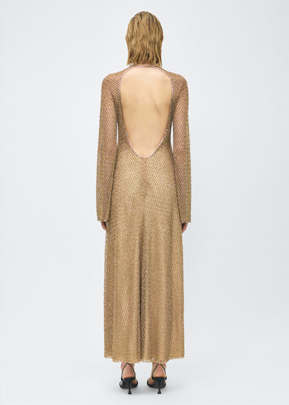 Model facing back, Image of the Sylvia Dress in Gold, P25 Adam Lippes collection; The Sylvia Dress in gold glass beaded tulle features intricate hand-beading, a process that takes multiple days, arranged in the signature diamond motif pattern for a striking visual effect. Designed with an elegant open back and a detachable cami, this dress offers versatile styling options with maximum impact.