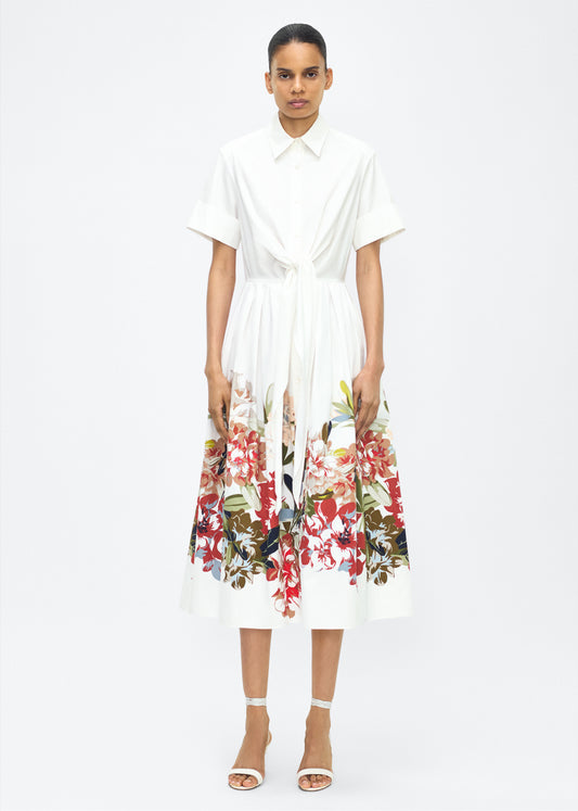 Model facing front, Attacher Dress in white multi, P25 Collection from Adam Lippes; Our classic Attacher silhouette returns, crafted from Italian cotton poplin and printed with this season’s Sicily-inspired floral motif. Featuring side pockets and diamond monogram mother of pearl buttons, the attached waist sash can be tied at the front or back to cinch the waist.