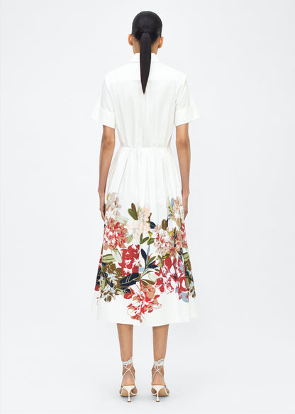 Model facing back, Attacher Dress in white multi, P25 Collection from Adam Lippes; Our classic Attacher silhouette returns, crafted from Italian cotton poplin and printed with this season’s Sicily-inspired floral motif. Featuring side pockets and diamond monogram mother of pearl buttons, the attached waist sash can be tied at the front or back to cinch the waist.
