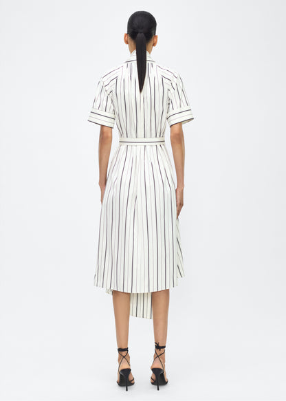 Model facing back, P25723SS, Ivory/Black, P25 Adam Lippes collection: The Nansi Dress is crafted from crisp stripe poplin in ivory and black, featuring an asymmetrical hem that adds a modern twist to a classic design. A sleek V-neckline and short sleeves enhance its effortless sophistication, while a fabric belt cinches the waist for a defined silhouette.