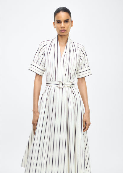Model facing front, P25723SS, Ivory/Black, P25 Adam Lippes collection: The Nansi Dress is crafted from crisp stripe poplin in ivory and black, featuring an asymmetrical hem that adds a modern twist to a classic design. A sleek V-neckline and short sleeves enhance its effortless sophistication, while a fabric belt cinches the waist for a defined silhouette.