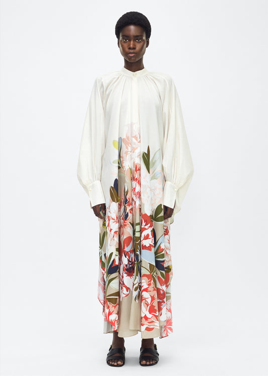 Model facing front, P25726PV,  Rysa Caftan, Champagne/Multi, Adam Lippes P25 Collection; A new shape from the atelier, the Rysa Caftan is crafted from airy printed voile, featuring this season’s Sicily-inspired floral motif. The fluid hem adds a modern twist to the traditional caftan silhouette. With its flowing, relaxed fit, it exudes effortless elegance. Features a button loop closure and diamond monogram mother of pearl buttons.