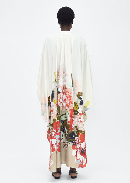 Model facing back, P25726PV,  Rysa Caftan, Champagne/Multi, Adam Lippes P25 Collection; A new shape from the atelier, the Rysa Caftan is crafted from airy printed voile, featuring this season’s Sicily-inspired floral motif. The fluid hem adds a modern twist to the traditional caftan silhouette. With its flowing, relaxed fit, it exudes effortless elegance. Features a button loop closure and diamond monogram mother of pearl buttons.