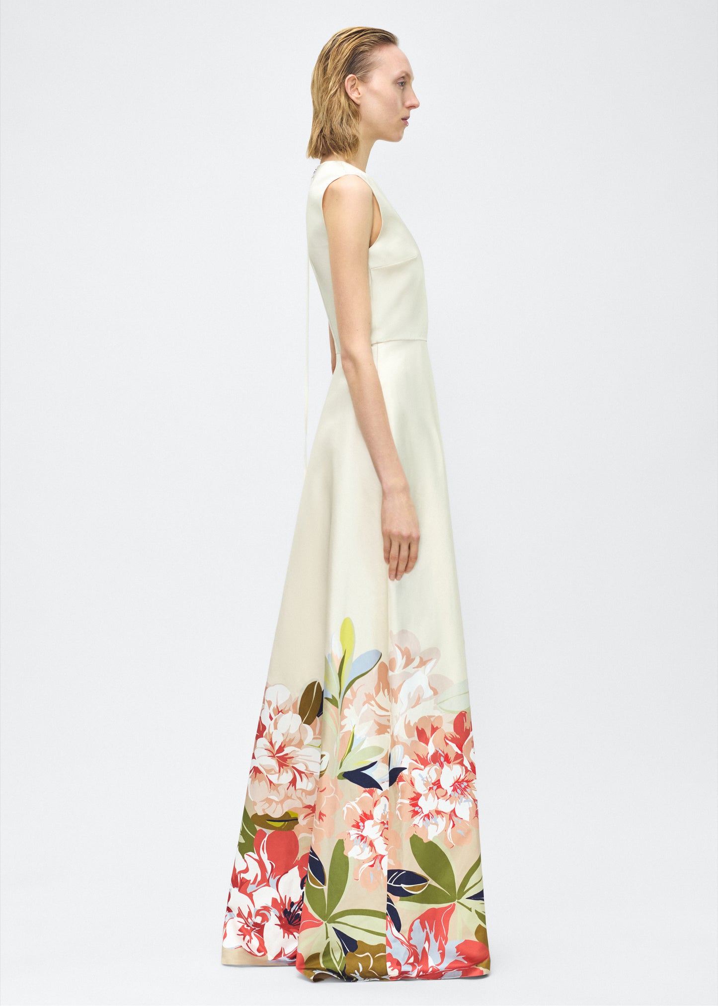 Image of model facing side – Alienor Dress, P25731PU, Champagne/Multi – Adam Lippes, P25 collection: The Alienor Dress in printed duchess satin is defined by its elegant simplicity. Adorned with the Pre-Fall collection’s Sicily-inspired floral motif, it features a classic rounded neckline and flows gracefully for effortless wear.