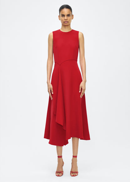 Model facing front– Lynn Dress, P25753SE, Poppy – Adam Lippes, P25 collection: The Lynn Dress introduces a striking new silhouette in silk crepe. This sleeveless design features a softly contoured waistline and an asymmetric draped panel, creating a dynamic and effortless shape.