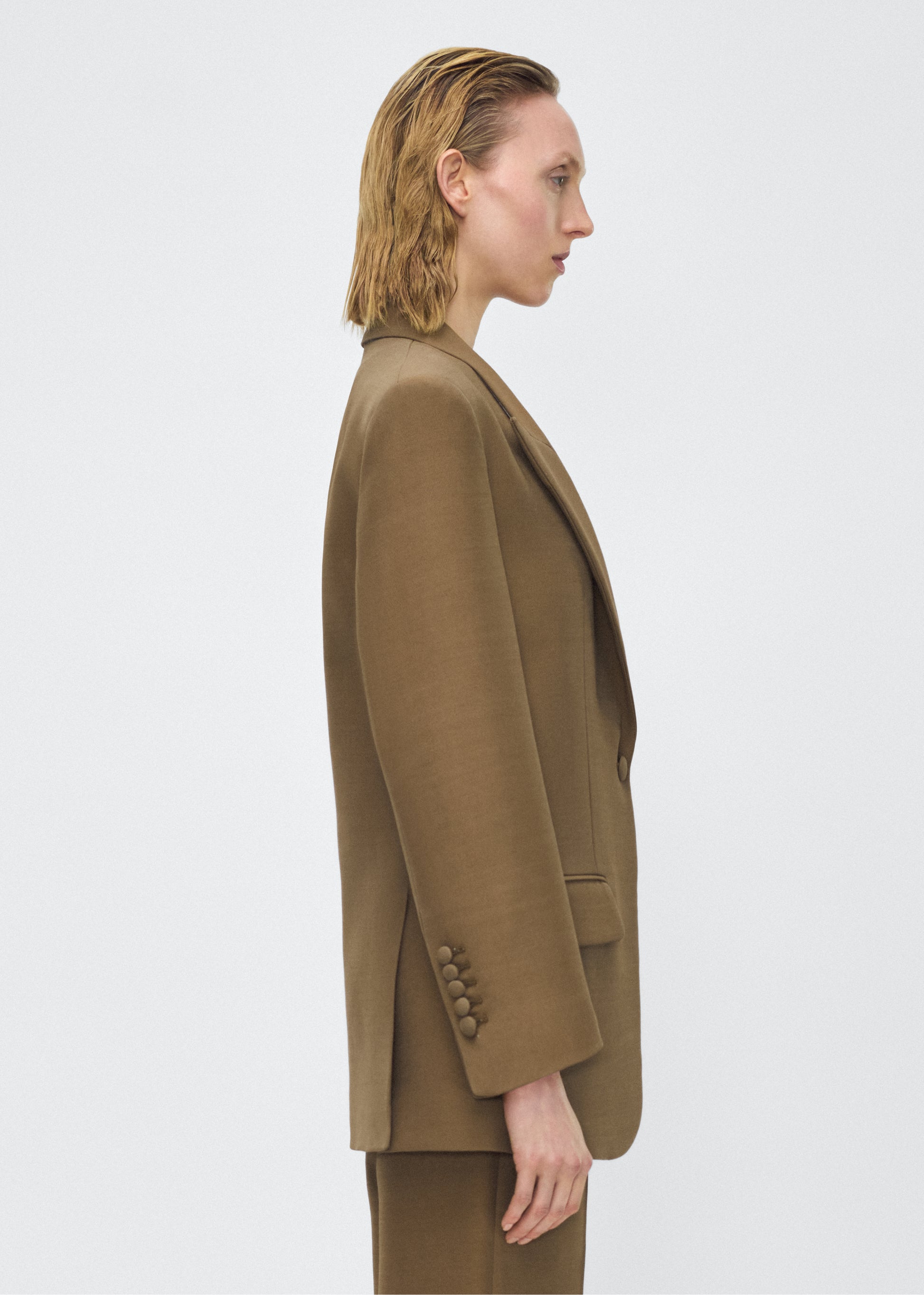 Model facing side, wearing the brody jacket in military green color, Adam Lippes P25 collection, A signature shape from the atelier, the Brody Jacket is crafted from luxurious silk wool, offering a soft yet structured silhouette. Designed with a single button closure, front pockets, and a sleek notched collar, this jacket effortlessly elevates any ensemble.