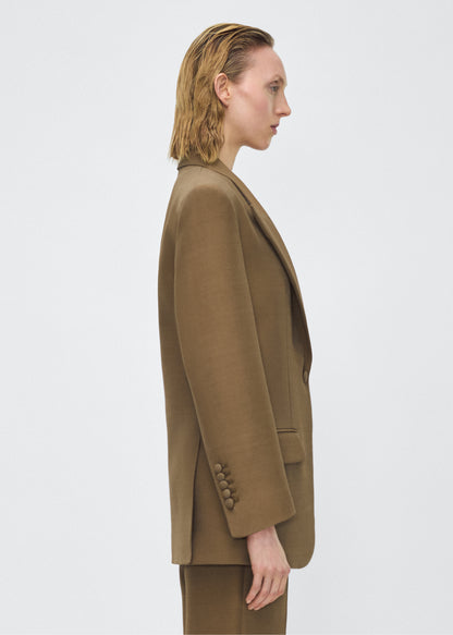 Model facing side, wearing the brody jacket in military green color, Adam Lippes P25 collection, A signature shape from the atelier, the Brody Jacket is crafted from luxurious silk wool, offering a soft yet structured silhouette. Designed with a single button closure, front pockets, and a sleek notched collar, this jacket effortlessly elevates any ensemble.