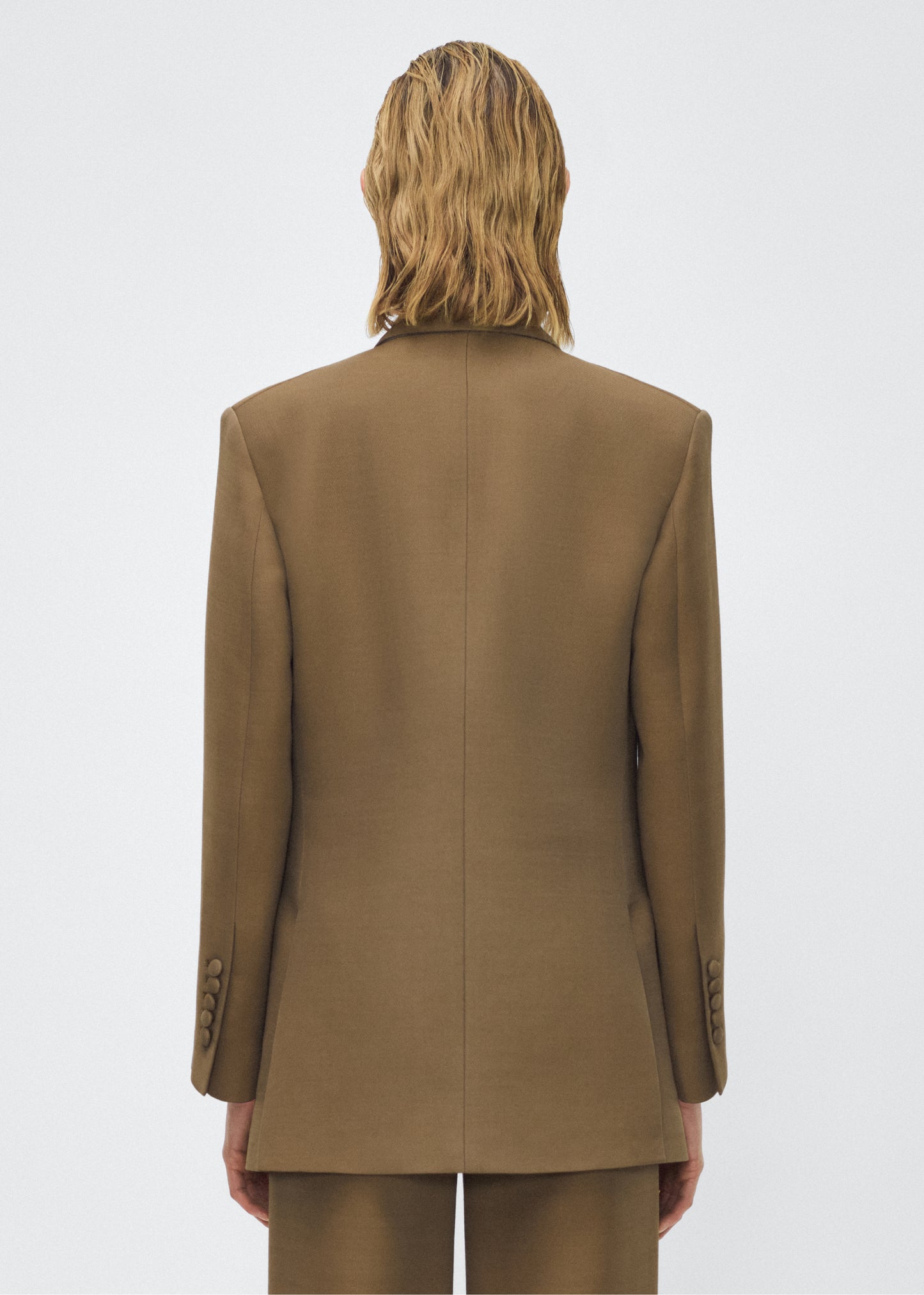 Model facing back, wearing the brody jacket in military green color, Adam Lippes P25 collection, A signature shape from the atelier, the Brody Jacket is crafted from luxurious silk wool, offering a soft yet structured silhouette. Designed with a single button closure, front pockets, and a sleek notched collar, this jacket effortlessly elevates any ensemble.