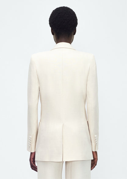 Image of model facing back – Riva jacket, P25805TR, ivory – Adam Lippes, P25 collection: Crafted in stretch canvas with a refined, lightweight structure, the Riva Jacket blends sharp tailoring with ease. Peaked lapels and a double-breasted front are punctuated by covered buttons for a clean, elegant finish.
